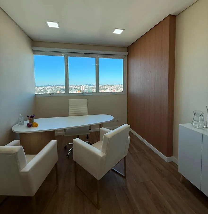 Sala de atendimento da Giullia: mesa branca, duas poltronas e janela ampla com vista da cidade